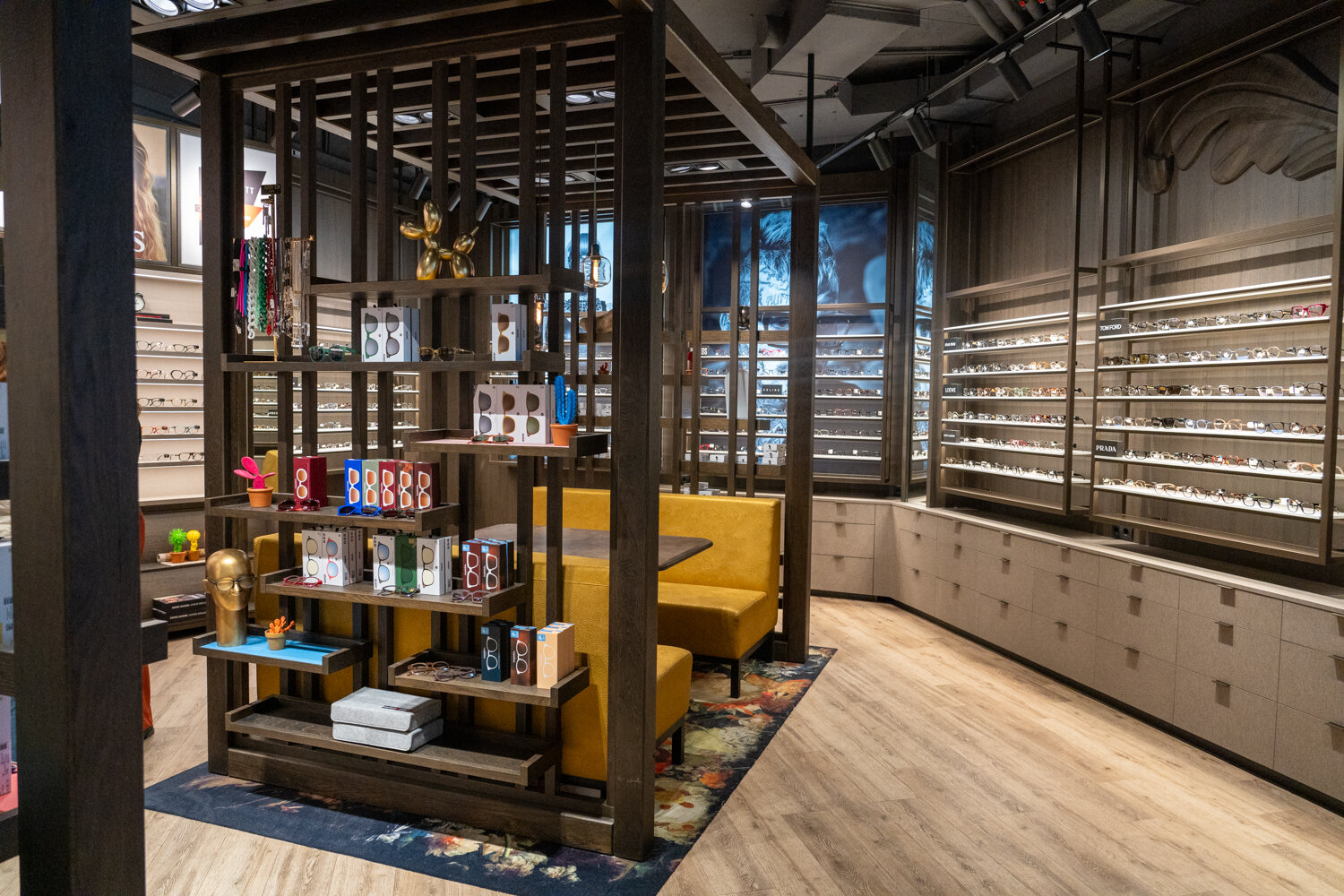 Innenansicht von Miller United Optics mit Holzregalen, gelber Lounge-Sitzbank, Parkettboden und beleuchteten Brillenwänden.