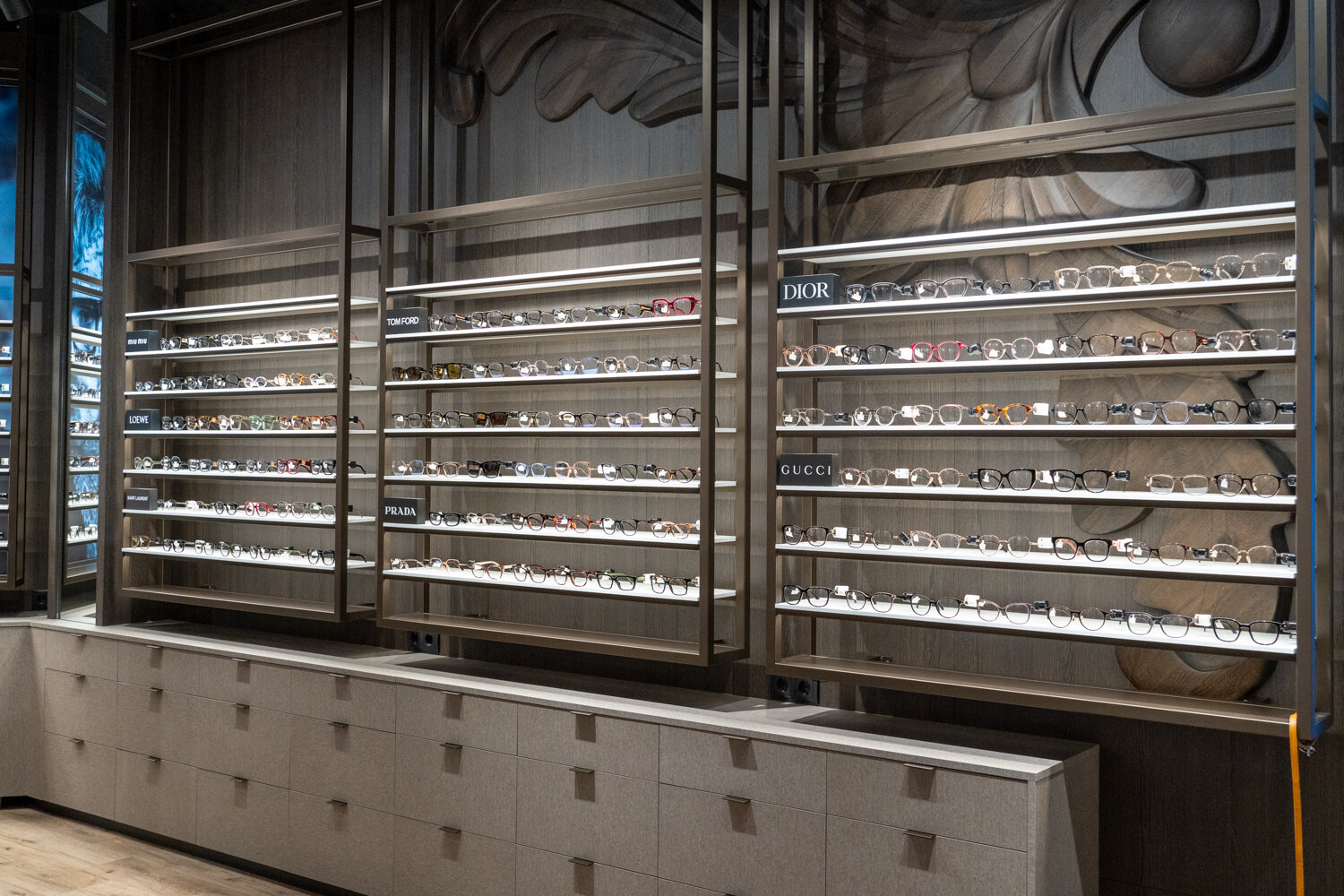 Eleganter Verkaufsbereich bei Miller United Optics mit großen Wandregalen für Korrekturbrillen von Marken wie Tom Ford, Prada, Dior und Gucci.