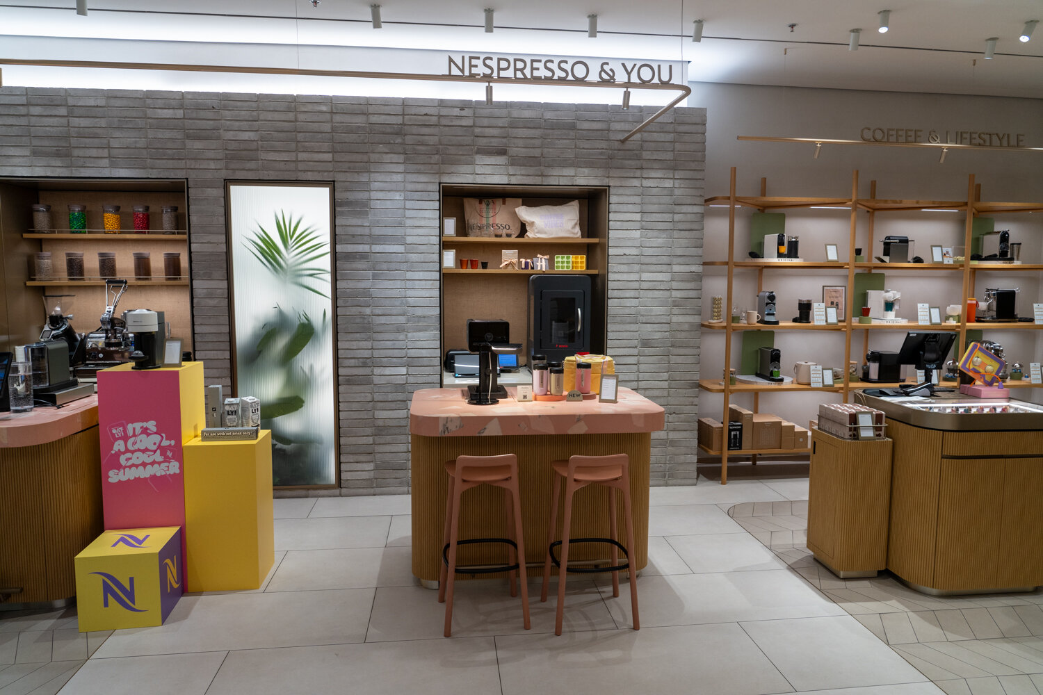 Modern gestalteter Nespresso-Verkaufsraum mit Verkostungstisch, Holzregalen für Kaffeemaschinen und hellem Steinmuster.