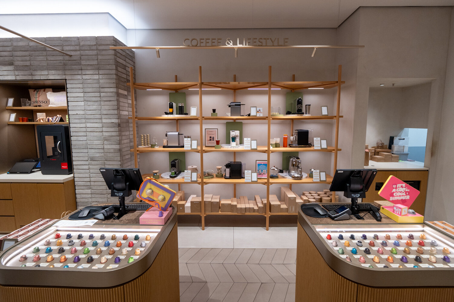 Kassenbereich der Nespresso Boutique mit gläsernen Kapselvitrinen und einem großen Wandregal voller Kaffeemaschinen.