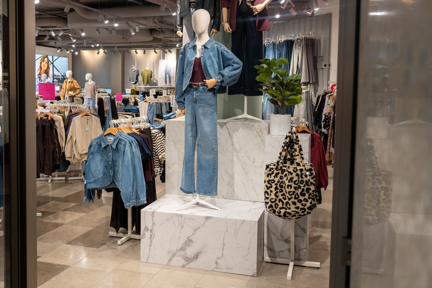Schaufensterpuppe auf Marmorsockel im ONLY Store mit Denim-Look aus Jeansjacke und Jeanshose sowie einer Tasche im Leopard-Muster.