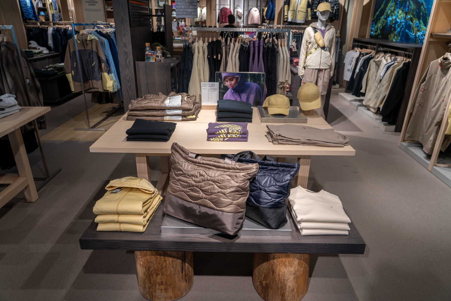 Präsentationstisch bei Peak Performance mit gefalteter Outdoor-Bekleidung, Stepptaschen, Caps und Schaufensterpuppen im Hintergrund.