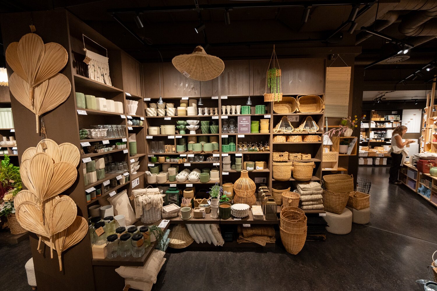 Dunkle Holzregale bei Søstrene Grene mit Flechtkörben, Blumentöpfen, Vasen und Dekorationsartikeln aus Naturmaterialien.