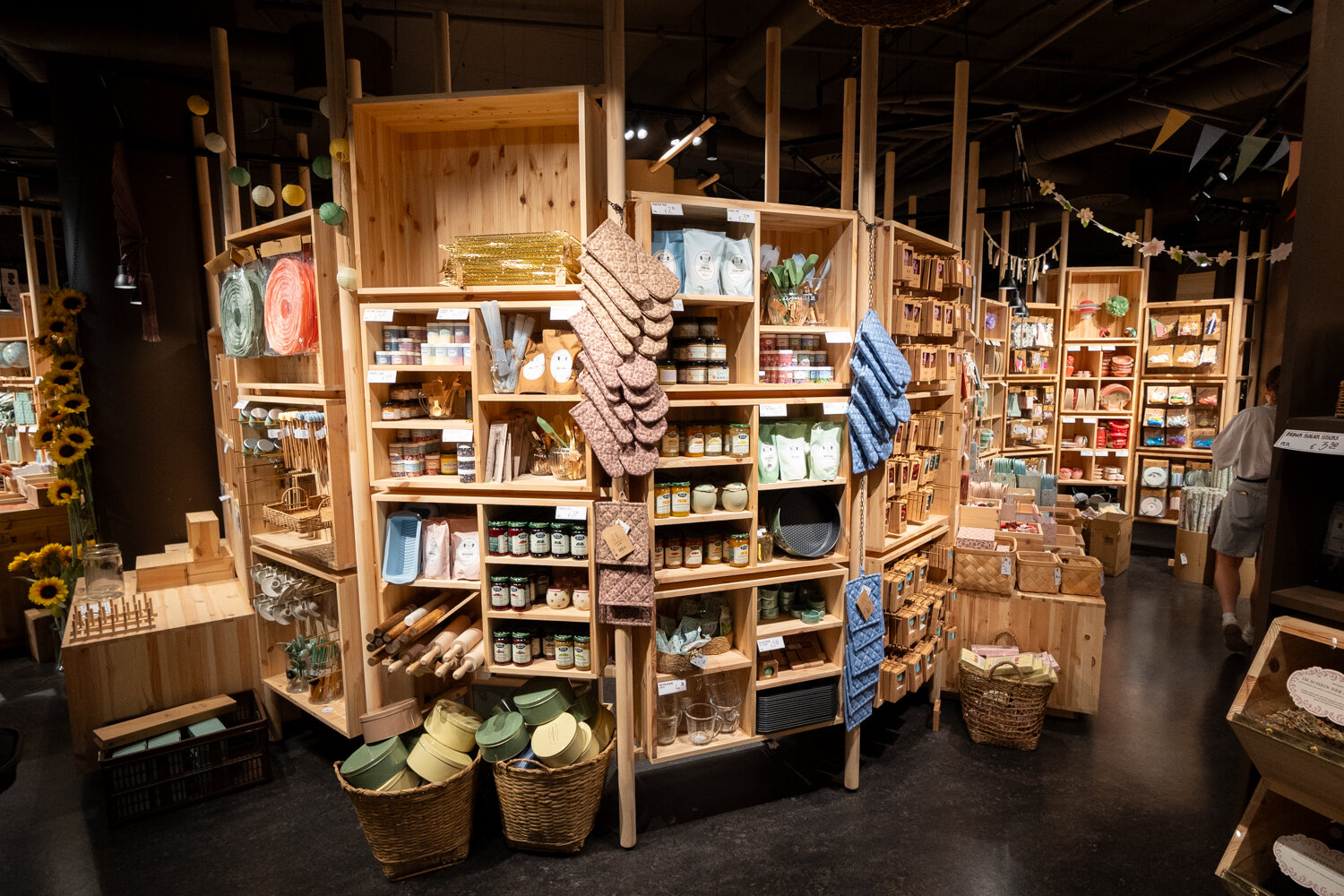 Verkaufsregale aus hellem Holz bei Søstrene Grene mit Küchenutensilien, Vorratsgläsern, Backzubehör und Dekoartikeln.