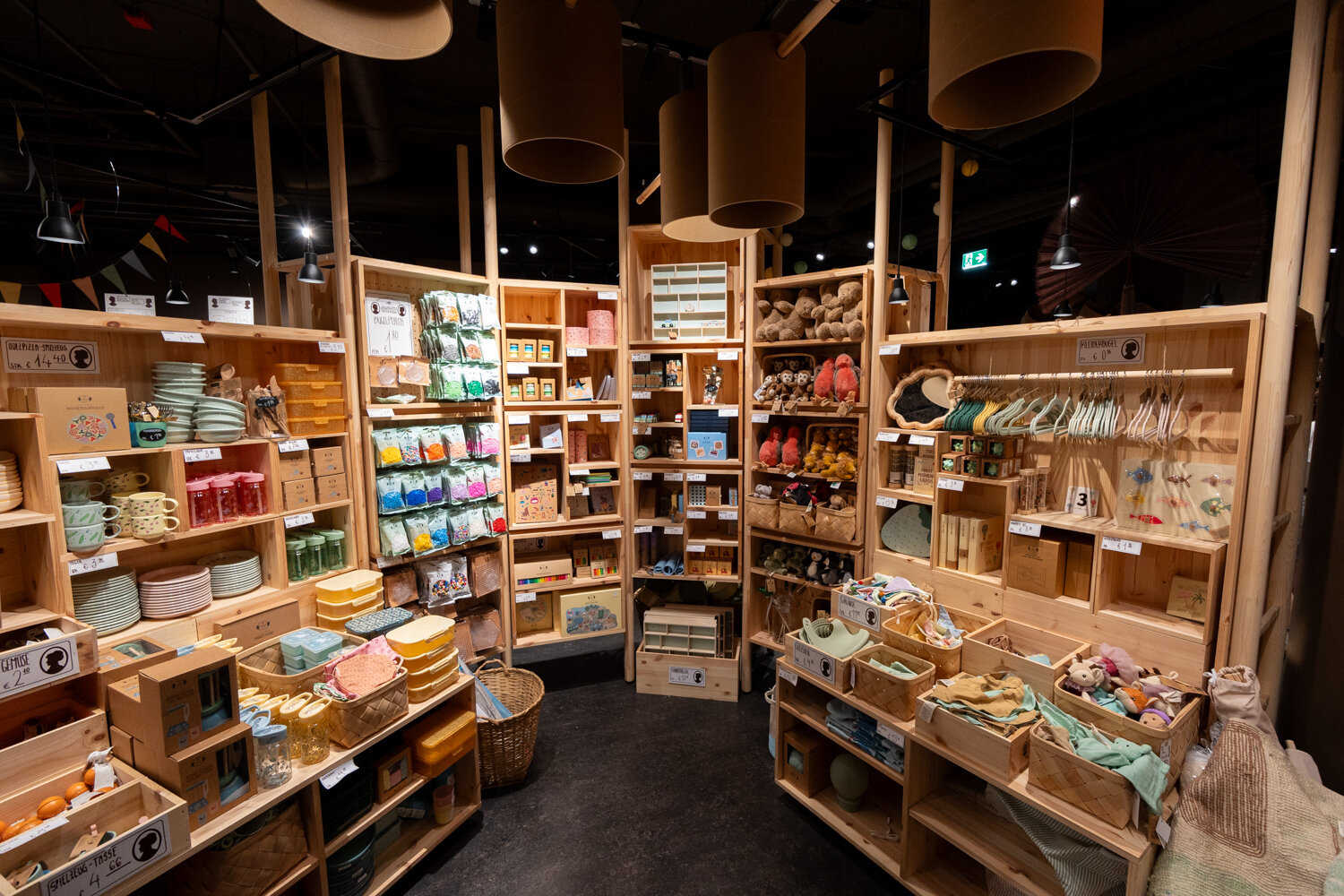 Verkaufsbereich bei Søstrene Grene mit Kindergeschirr, Holzspielzeug, Plüschtieren und Bastelbedarf in Holzregalen.