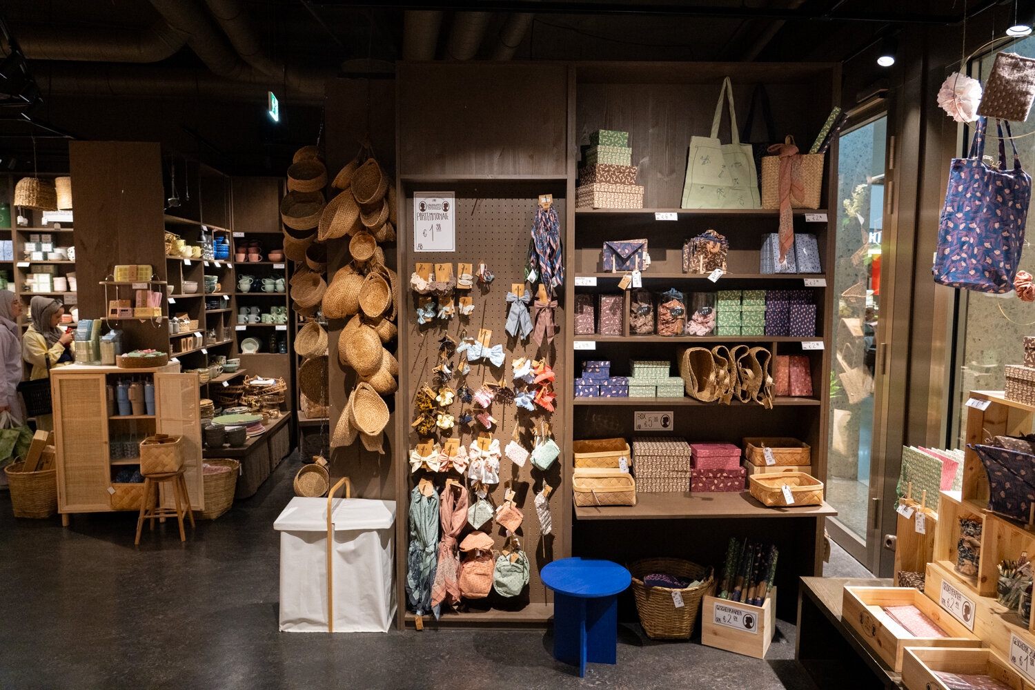 Verkaufsbereich bei Søstrene Grene mit Flechtkörben, Haaraccessoires, Geschenkboxen und Stofftaschen im dunklen Holzregal.