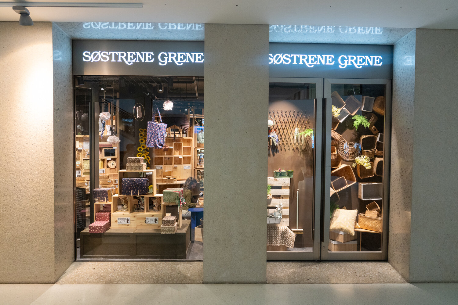 Schaufensterfront und Eingang des Søstrene Grene Stores im Einkaufszentrum mit dekorativ arrangierten Kisten, Körben und Geschenkboxen.