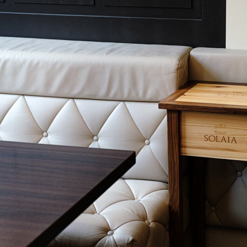 Elegante, cremefarbene Leder-Sitzbank mit stilvoller Knopfheftung neben einem dunklen Holztisch.