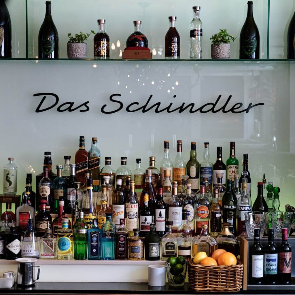Gut bestücktes Barregal mit zahlreichen Spirituosen, dem Marken-Schriftzug an der Wand und frischen Zitrusfrüchten.