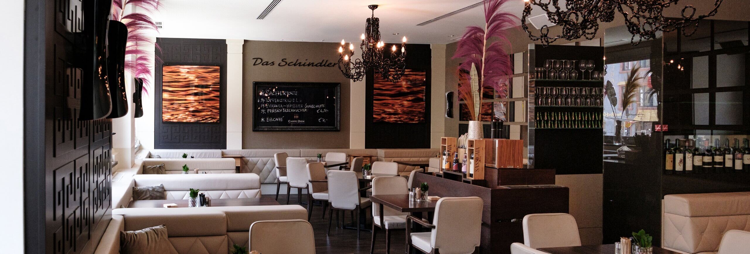 Stilvoller Gastronomiebereich im Restaurant Das Schindler mit eleganter Bestuhlung dunklem Parkett und Kronleuchtern an der Decke.