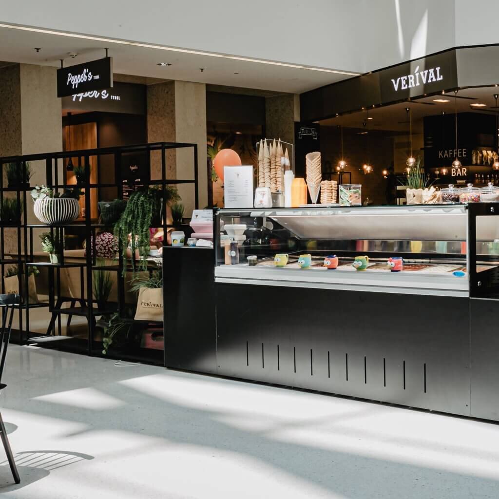 Moderner, schwarzer Eisstand von Sofia's Natureis im Kaufhaus Tyrol mit einer gläsernen Eisvitrine neben dem Verival-Kaffeebereich.