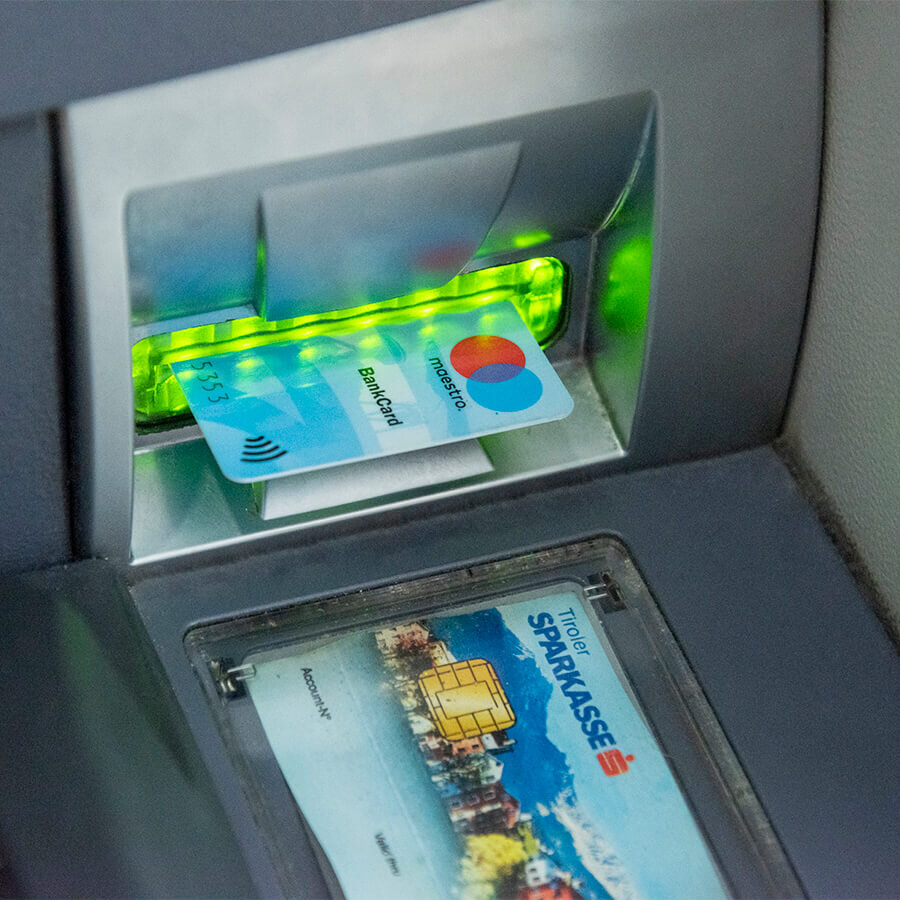 Nahaufnahme einer blauen Bankkarte, die in den grün leuchtenden Kartenschlitz eines Sparkassen-Geldautomaten eingeführt wird.