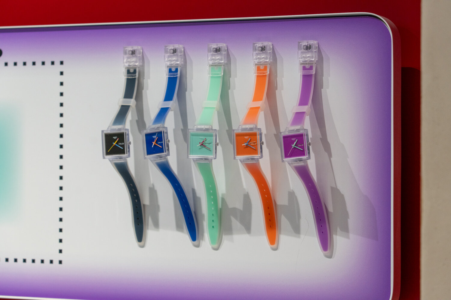 Wanddisplay mit fünf viereckigen Swatch-Uhren in verschiedenen Farben.