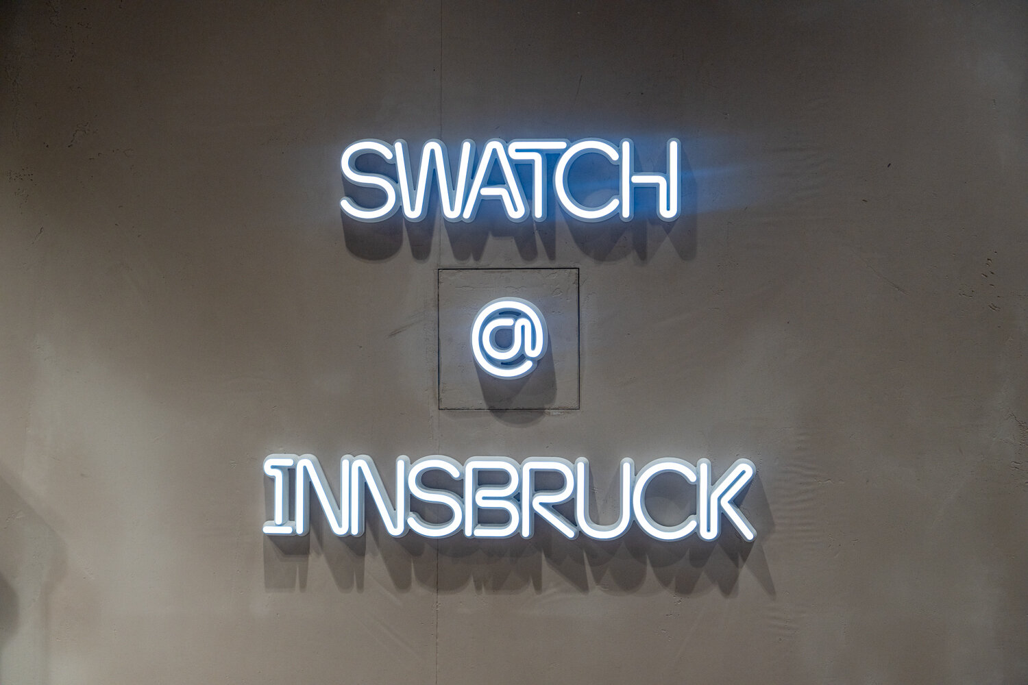 Beleuchtete Neon-Schrift an einer Betonwand mit dem Text Swatch @ Innsbruck.