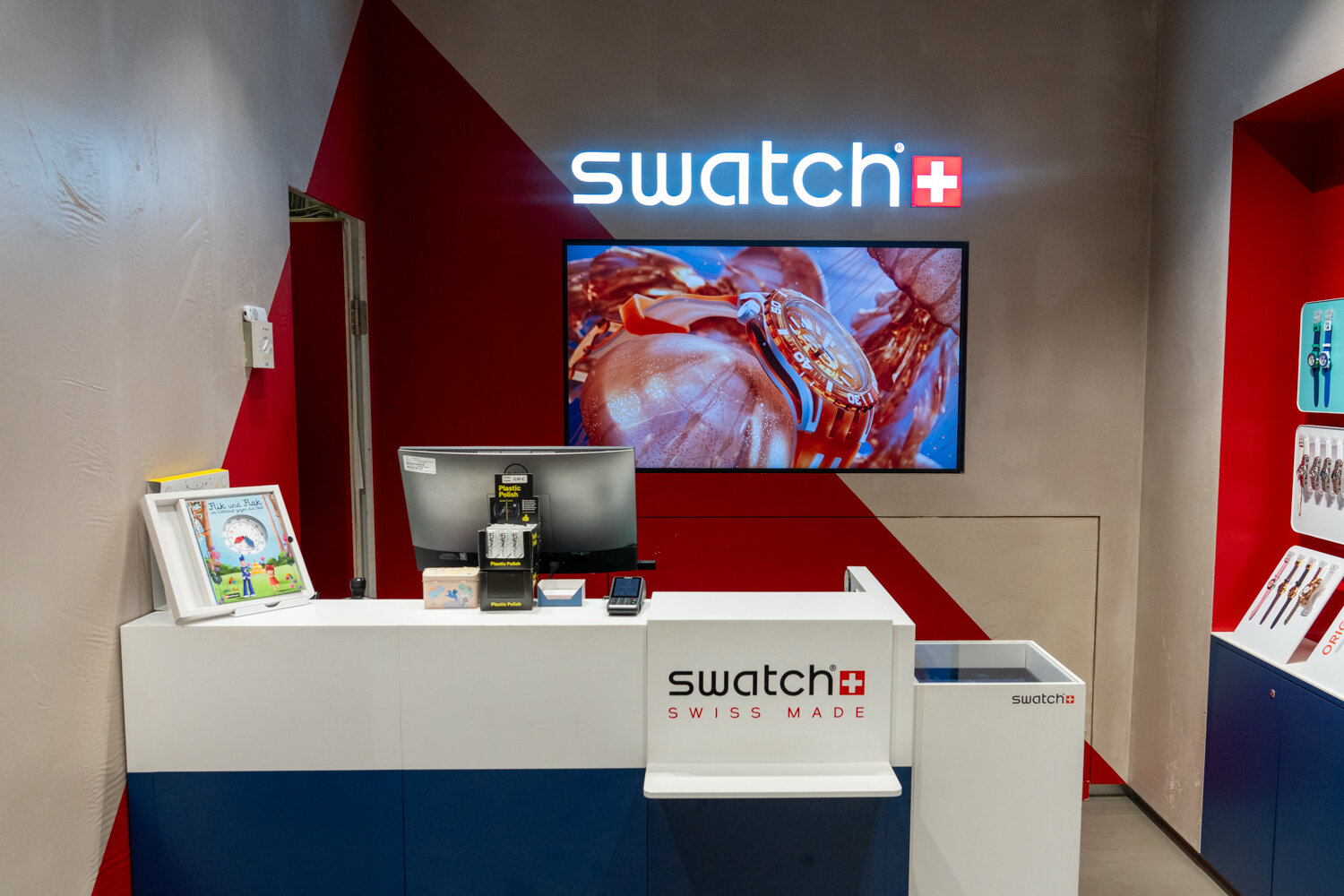 Kassenbereich des Swatch Stores in blau-weiß-rot mit Markenlogo, Bildschirm und Uhrendisplay.
