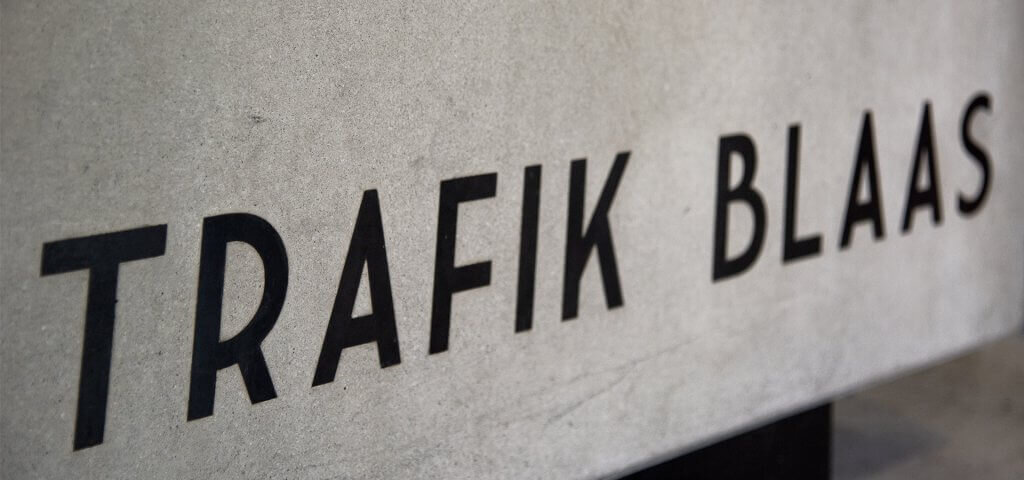 Nahaufnahme des markanten Schriftzugs „TRAFIK BLAAS“ in schwarzen Großbuchstaben auf einer grauen Betonoberfläche.