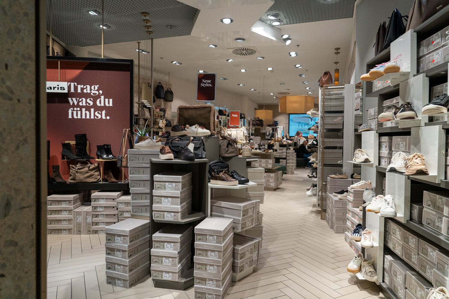 Hell gestalteter Innenraum des Tamaris Schuhgeschäfts mit Verkaufsregalen, Schuhkarton-Stapeln und Wandspruch Trag, was du fühlst.