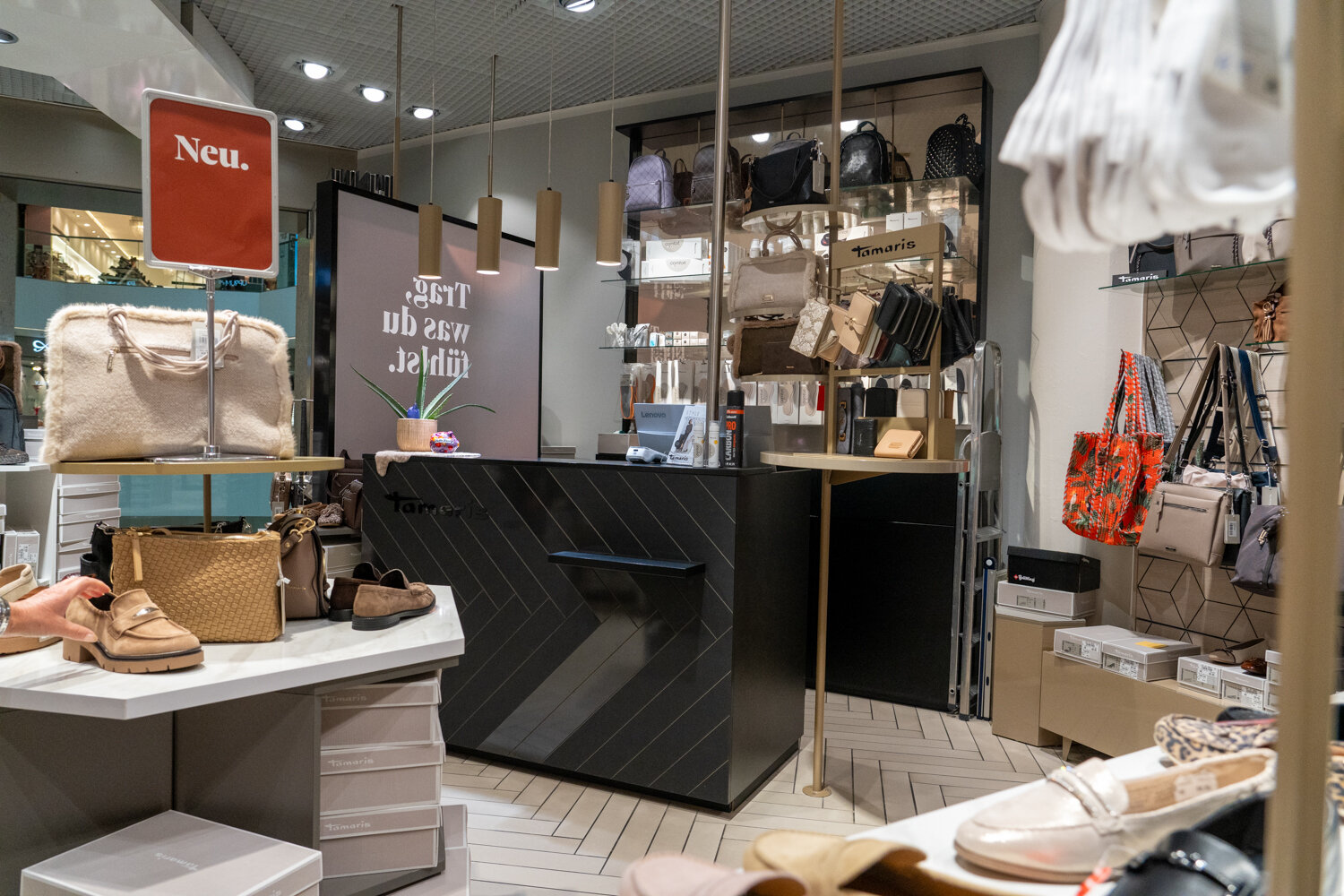 Schwarzer Kassenbereich im Tamaris Store mit Vorführung von Schuhen, Geldbörsen und Taschen auf Ständern.