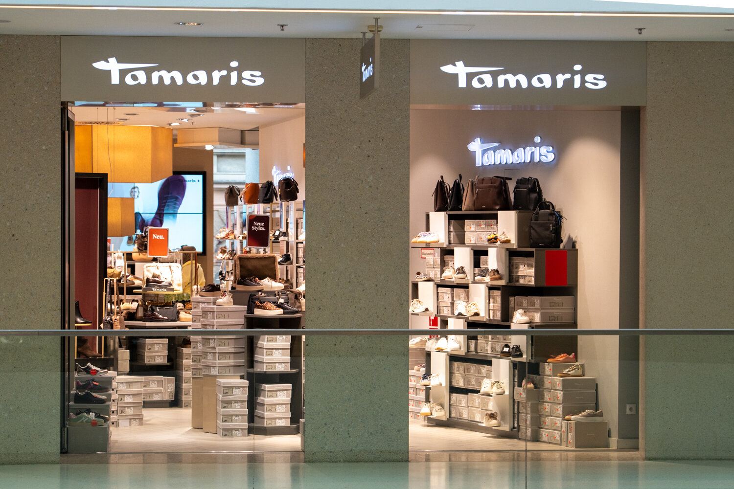 Außenansicht der Tamaris-Filiale im Einkaufszentrum mit zwei offenen Eingängen, beleuchtetem Logo und präsentierten Schuhkartons.
