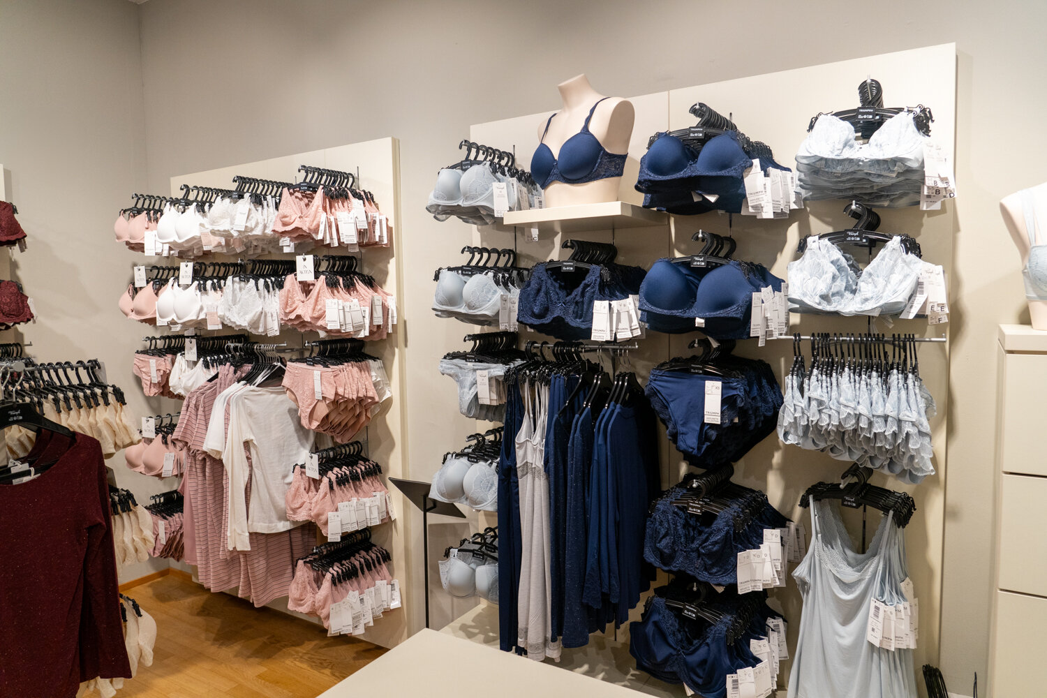 Wandpräsentation bei Triumph mit Unterwäsche, BHs und Slips in Rosé-, Hellblau- und Dunkelblautönen sowie BH-Büsten.