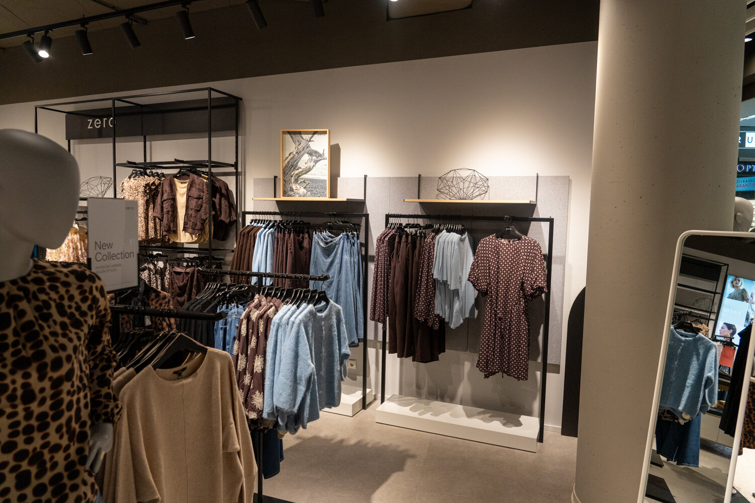 Verkaufsständer bei zero mit der neuen Kollektion, blauen Strickpullovern, Kleidern und einem Standspiegel im Hintergrund.