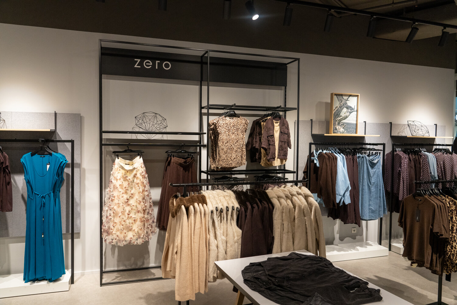 Kleiderständer und Wandregale bei zero mit Herbstmode, blauen Kleidern, Strickjacken und gefalteter Bekleidung.