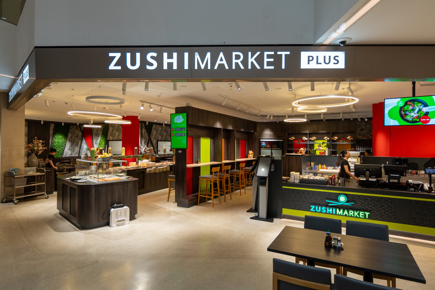 Eingangsbereich des Restaurants Zushi Market Plus mit Buffetstationen, Kassentheke und modernen Leuchten.